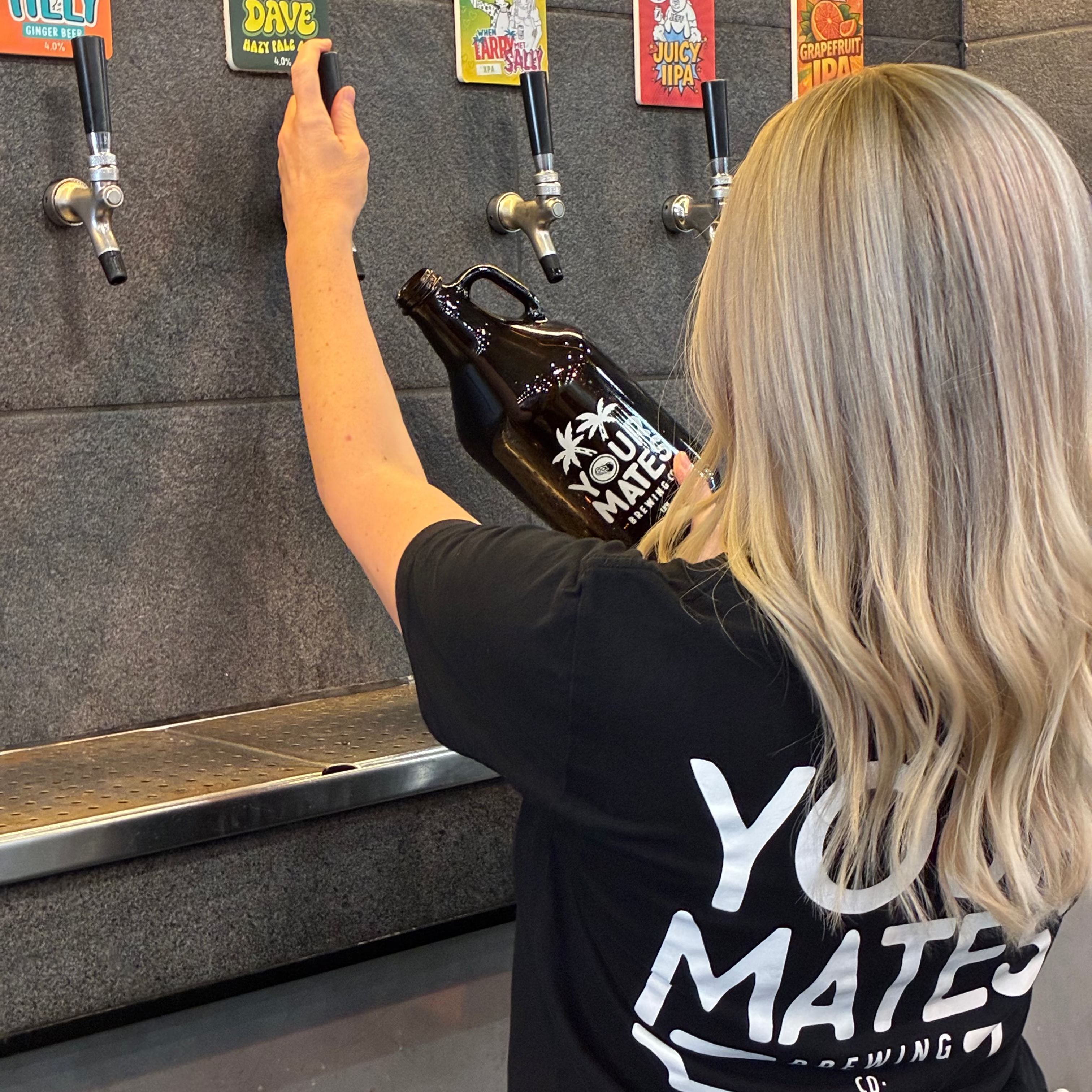 Person at a bar using a tap to fill a bottle with a branded shirt on.
