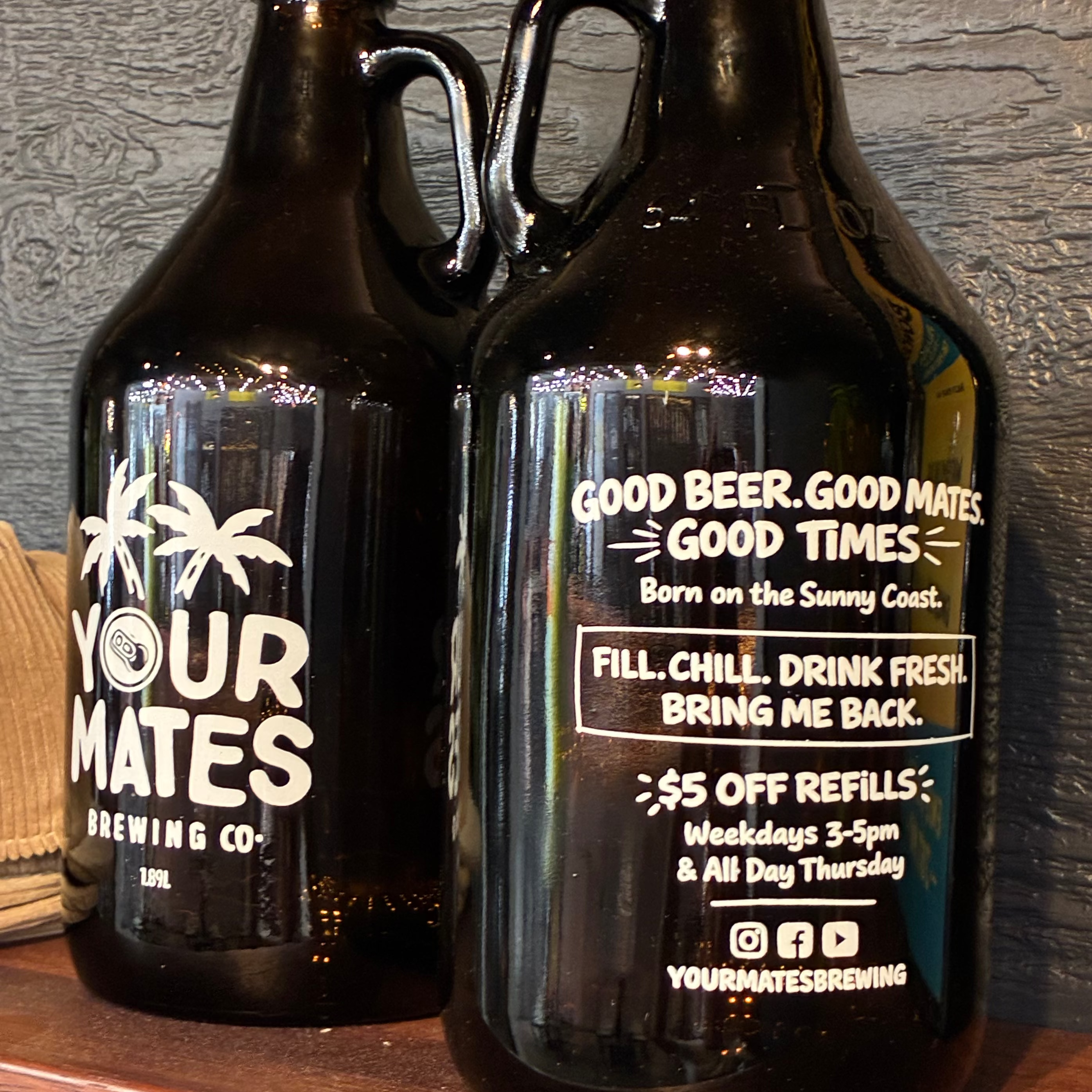 Two black growlers with white text on a wooden surface and gray wall background.
