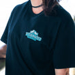 Load image into Gallery viewer, Person wearing a black t-shirt with a logo, standing outdoors.
