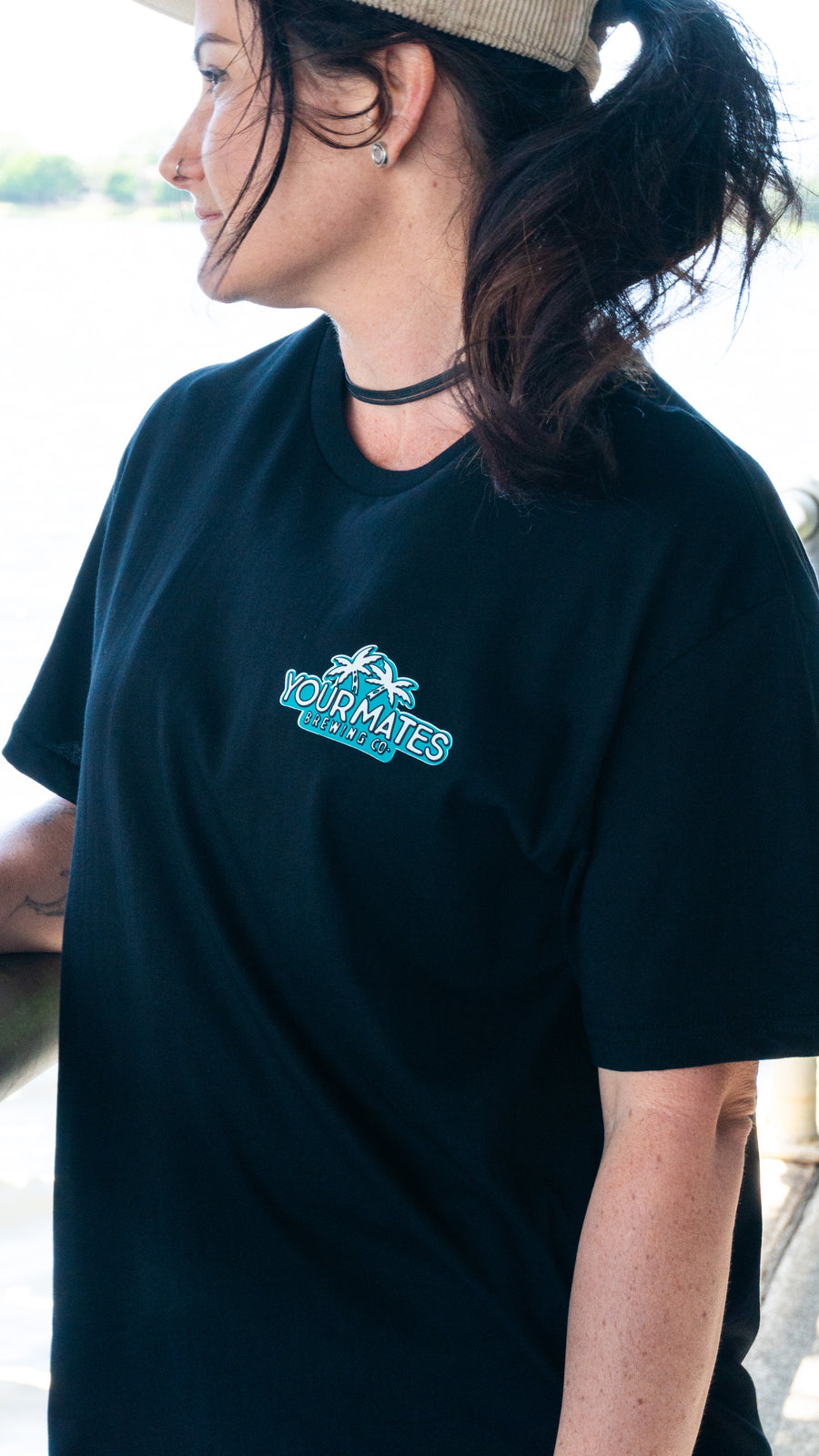 Person wearing a black t-shirt with a logo, standing outdoors.